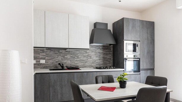 Una cocina moderna con armarios grises, una campana extractora negra, un microondas integrado y una estufa a gas. Hay una mesa de comedor con sillas y una planta en maceta.