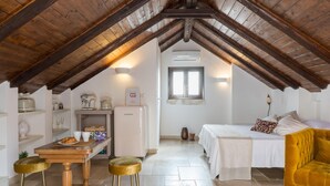 Ein gemütliches Schlafzimmer im Dachgeschoss mit Holzbalkendecke, einem Bett, einem kleinen Tisch mit Hocker und einer Küchenzeile.
