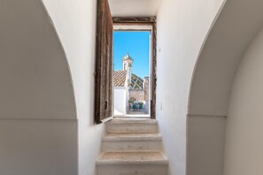 Eine schmale Treppe führt zu einer offenen Tür, von der aus man ein Gebäude mit einem Ziegeldach und einem Turm sieht.