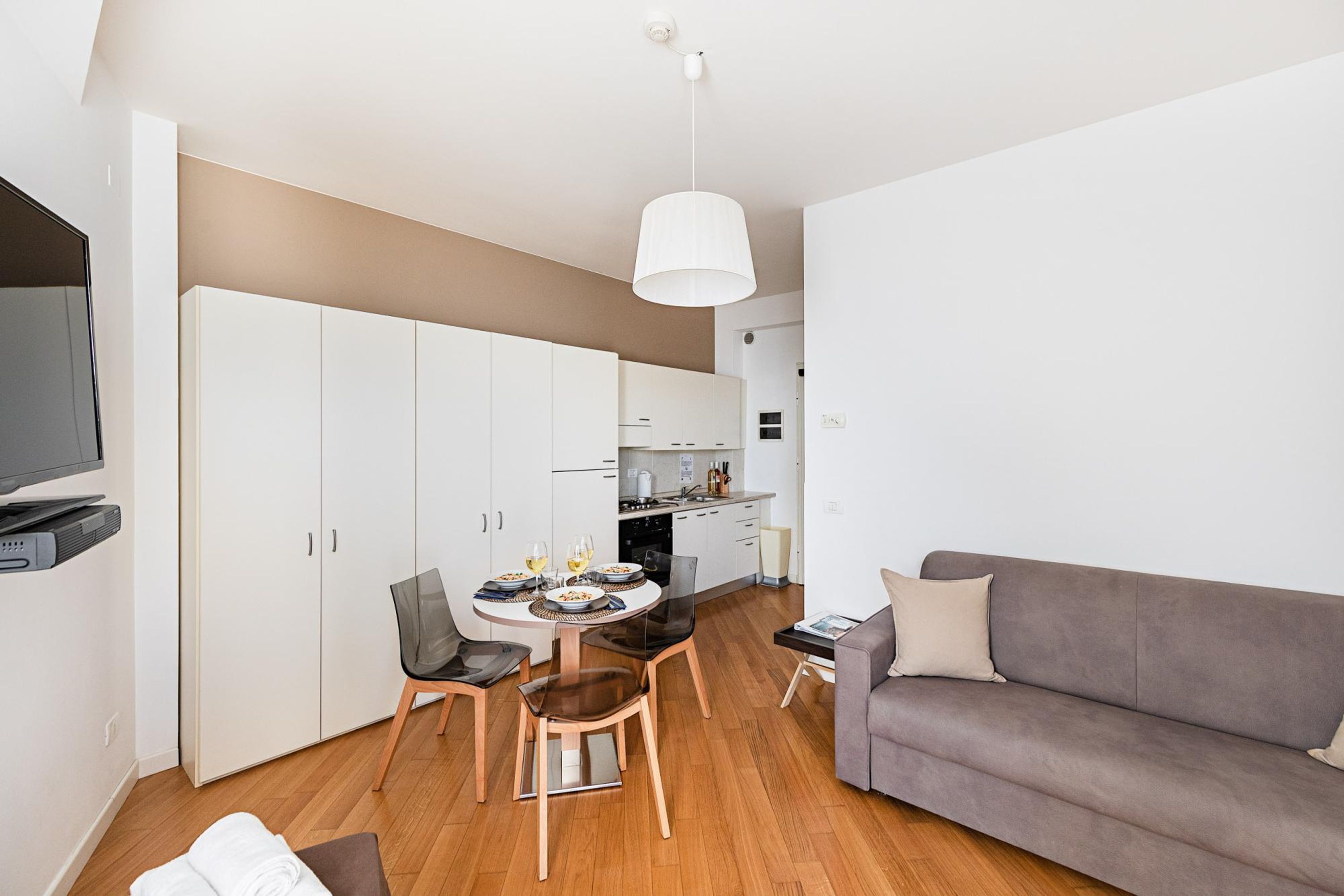 A modern living room with a grey sofa, a dining table with chairs, and a kitchen in the background.