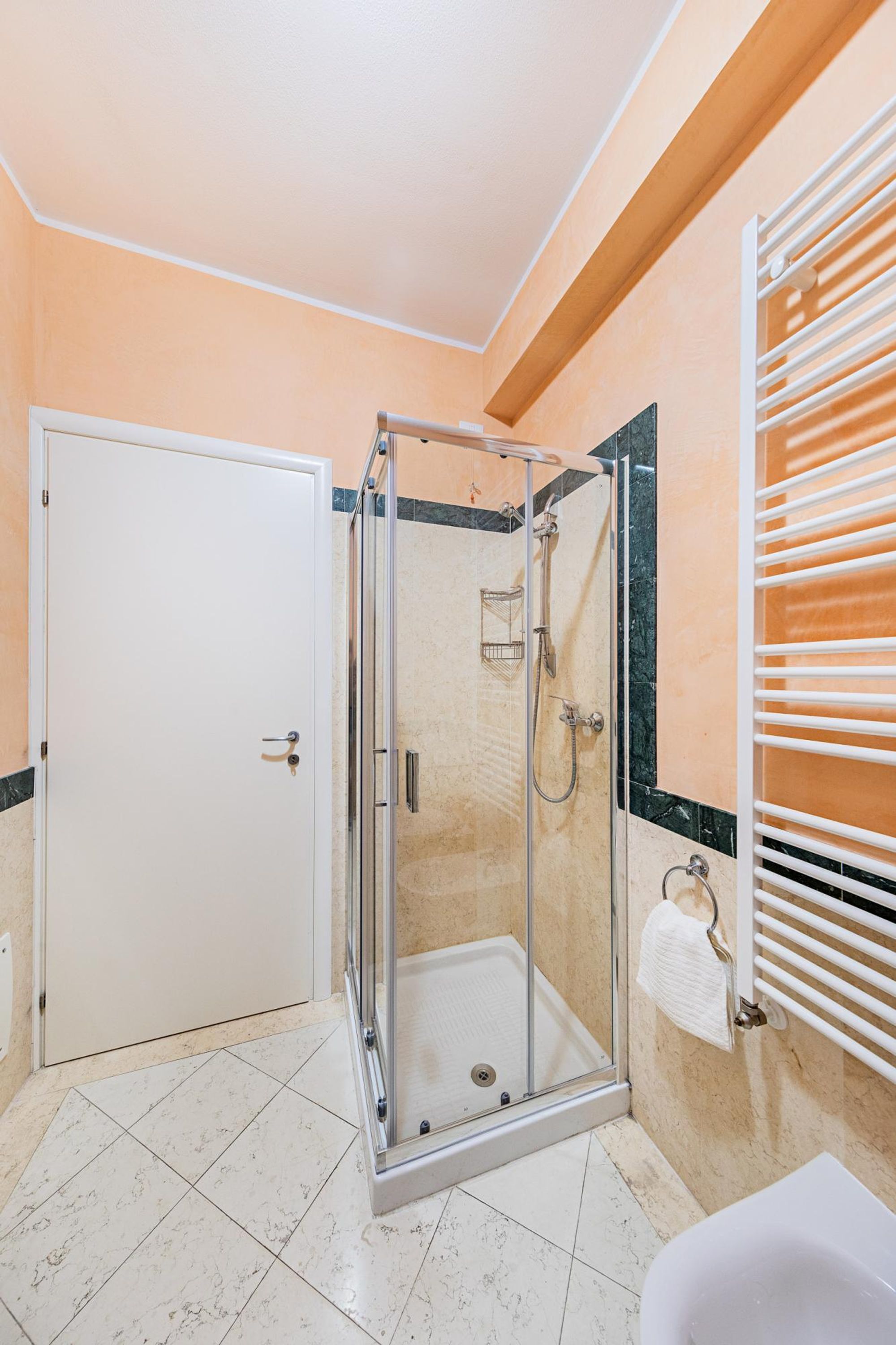 A bathroom with a glass-enclosed shower, a white door, a white sink, and a towel rack.