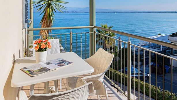A balcony with a table, chairs, a potted plant, and a view of the sea. - Residenza Miralago With Pool - Studio Apartment With Lake View (Desenzano del Garda)
