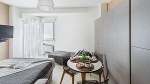 A modern hotel room with a bed, a dining table with breakfast, a TV, and a large wardrobe. - Residenza Miralago With Pool - Studio Apartment With Lake View (Desenzano del Garda)