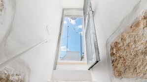 A narrow stairway leading to a window with a clear sky view, white walls, and a visible antenna. - Olivia in Wonderland by Wonderful Italy (Ostuni)
