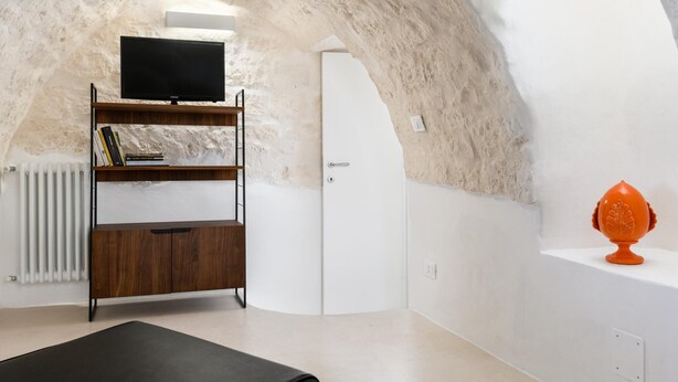 A modern interior with a stone wall, a wooden bookshelf, a white door, and a small orange decorative item. - Olivia in Wonderland by Wonderful Italy (Ostuni)