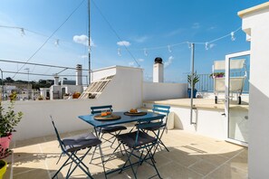 Une terrasse sur le toit, avec une table et des chaises, une vue sur la ville et des guirlandes lumineuses.