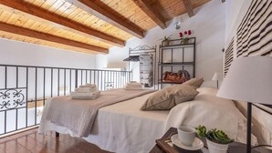 A bedroom with two beds, a wooden ceiling, a balcony, a metal shelf with towels, a lamp, and a small potted plant. - Salomone Apartment 15 With Terrace by Wonderful Italy (Syracuse)