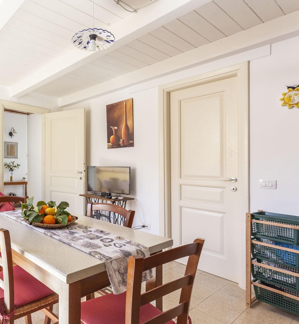 A dining area with a table set for two, chairs, a television, and a painting on the wall.