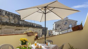 A table with a tablecloth, a glass of orange juice, a plate with croissants, and a potted plant with yellow flowers. - Salomone Apartment 15 With Terrace by Wonderful Italy (Syracuse)