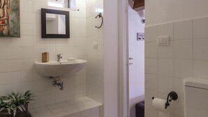 A bathroom with a white sink, mirror, and toilet. There is a wooden bench and a potted plant. - Salomone Apartment 15 With Terrace by Wonderful Italy (Syracuse)