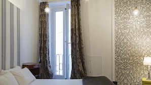 A bedroom with a bed, a nightstand, a door with curtains, a patterned wall, and a lamp on a side table. - La Dimora del Ducale by Wonderful Italy (Genoa)