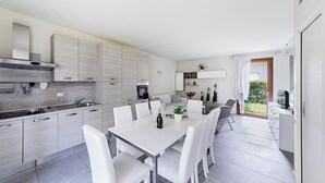 Uma cozinha moderna com armários brancos, uma mesa de jantar com cadeiras e um forno embutido.