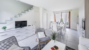 Um apartamento moderno com sala de estar, área de jantar e cozinha. Há uma escada que leva a outro nível, uma televisão de tela plana e uma mesa de jantar com cadeiras.