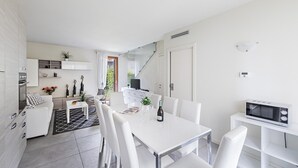 Cozinha moderna com armários brancos, área de refeições com mesa e cadeiras brancas, e micro-ondas embutido.