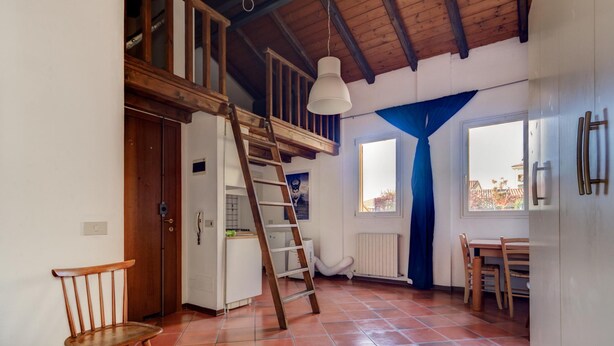 A kitchen with a wooden ceiling, a white pendant light, a wooden chair, a ladder, and a view through a window. - Nosadella Mezzanine by Wonderful Italy (Bologna)