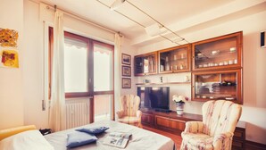 A hotel room with a bed, a television, a wooden cabinet with glass doors, and a window with curtains. - Le Orchidee 10 Apartment by Wonderful Italy (Sanremo)