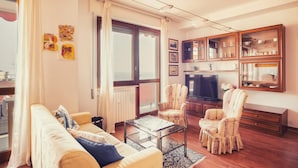 A living room with a sofa, armchairs, a coffee table, a television, and wooden cabinets. - Le Orchidee 10 Apartment by Wonderful Italy (Sanremo)