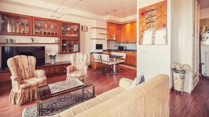 A modern living room with a sofa, armchairs, and a coffee table. There is a kitchen area with wooden cabinets and a dining table. - Le Orchidee 10 Apartment by Wonderful Italy (Sanremo)