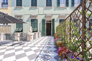 A checkered outdoor patio with a table and chairs, a statue, and a wooden trellis with flowers.