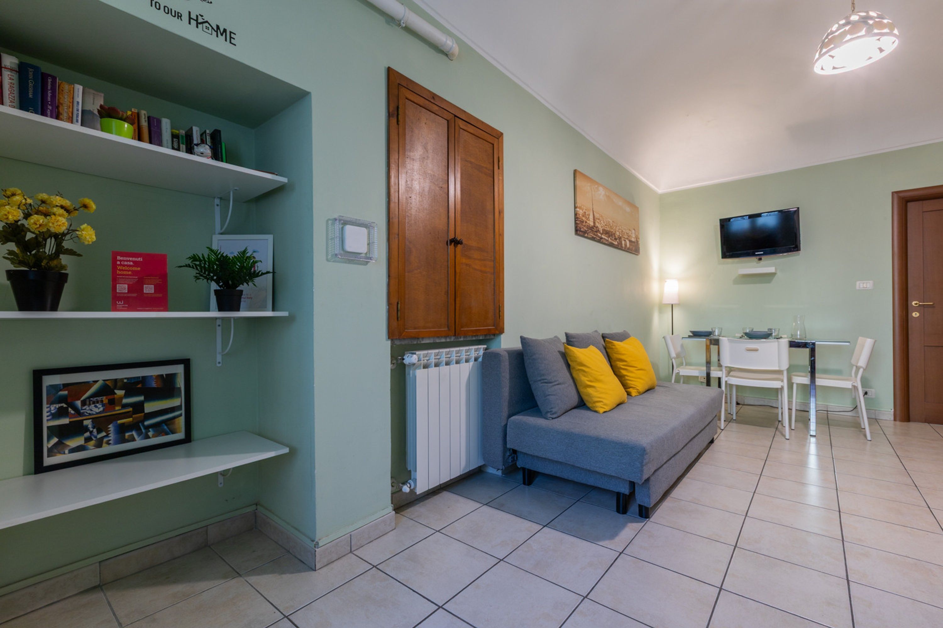 Un salon comprenant un canapé, un téléviseur, une table à manger avec des chaises, une bibliothèque et un radiateur.