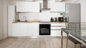 A modern kitchen with white cabinets, a stainless steel range hood, a built-in oven, a microwave, and a glass dining table. - Il Giardino Segreto di Orfeo by Wonderful Italy (Bologna)