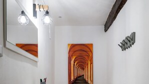 A hallway with a wooden floor, a white bench, a wall-mounted mirror, and a painting of an orange corridor. - Il Giardino Segreto di Orfeo by Wonderful Italy (Bologna)