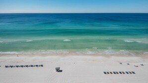 A beach with clear turquoise water, a sandy shore, and rows of beach chairs and umbrellas.