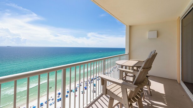 A balcony with a view of the ocean, a table, and chairs.