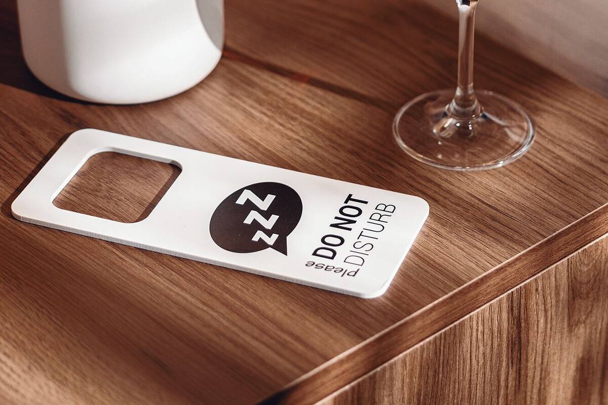 Una mesita de noche de madera con una lámpara blanca, una copa de vino y un cartel de 'no molestar'.