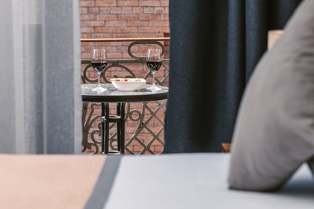Una mesa de comedor con dos copas de vino y un bol de comida, frente a un muro de ladrillo y una barandilla de metal.