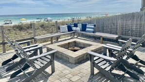 Een terras aan het strand met Adirondack-stoelen, een vuurplaats en uitzicht op de oceaan.