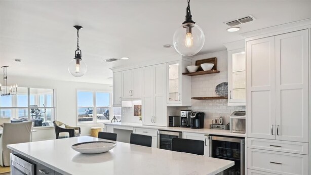 Een moderne keuken met witte kasten, een groot eiland en hanglampen.