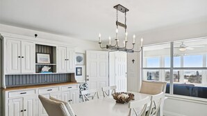 Een keuken met witte kastjes, een eettafel met stoelen, een kroonluchter en uitzicht door grote ramen.