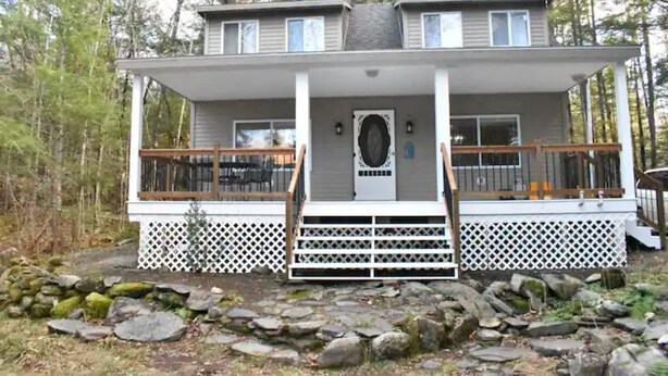 A two-story cabin with a front porch, a small deck, and a stone foundation. - Sebec Lake House (Dover-Foxcroft)