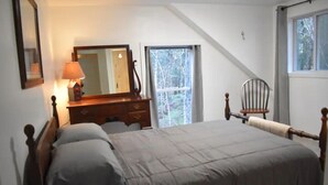 A bedroom with a bed, a dresser, a chair, a mirror, and a window. - Sebec Lake House (Dover-Foxcroft)