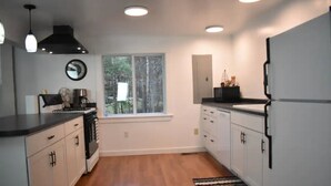 A modern kitchen with white cabinets, a black countertop, and a large window. - Sebec Lake House (Dover-Foxcroft)