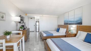 A hotel room with two beds, a desk, a chair, a refrigerator, and a TV.