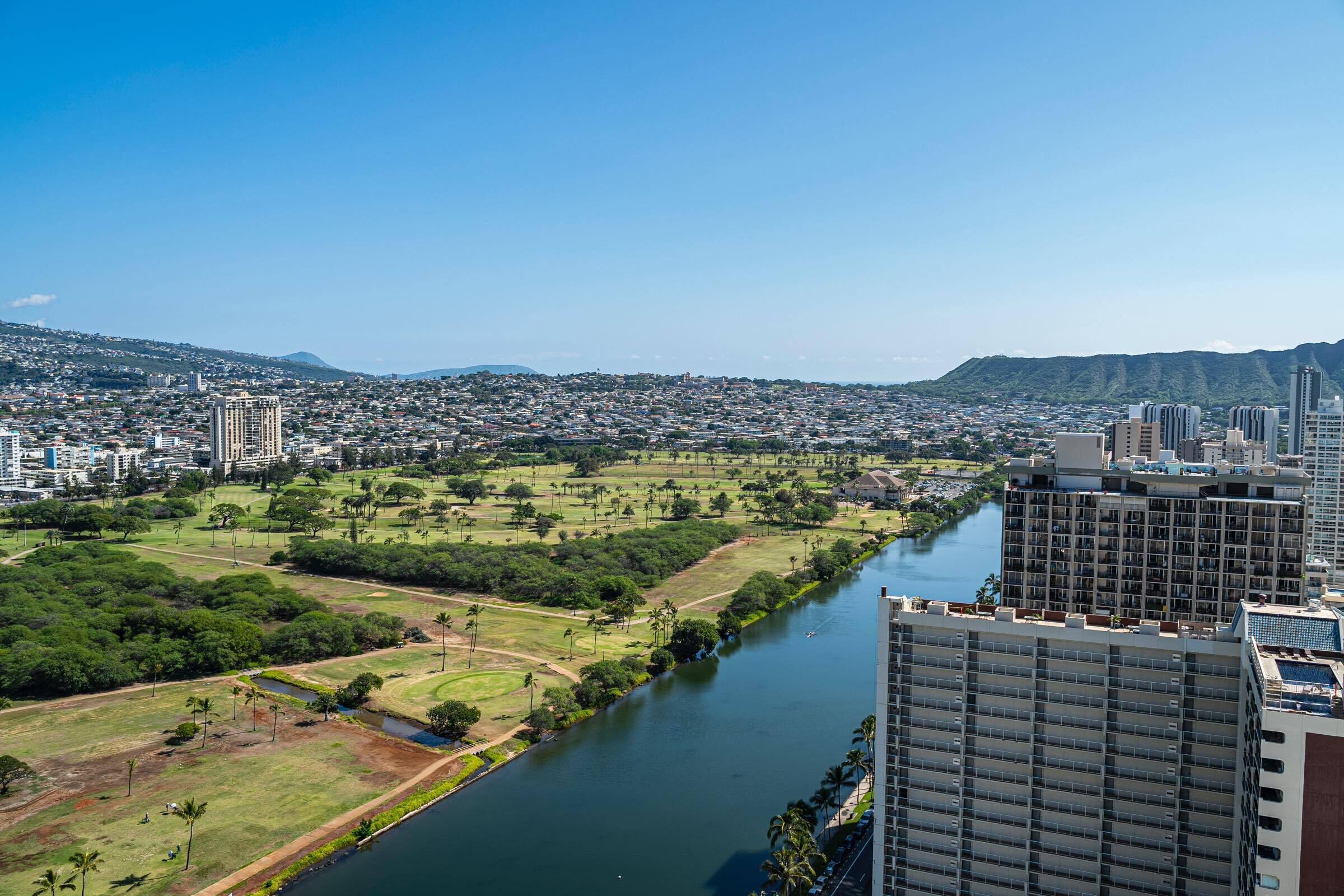 Un hôtel de grande hauteur surplombant une rivière, avec un parc et une vue sur la ville en arrière-plan.