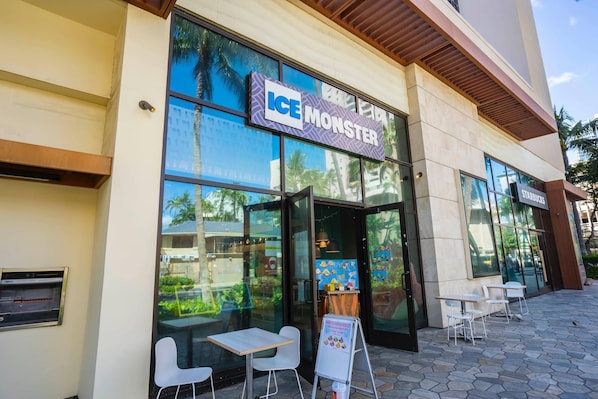 Exterior de un edificio con un letrero que dice "ICE MONSTER" y el logo de Starbucks. Hay áreas de estar al aire libre con mesas y sillas.