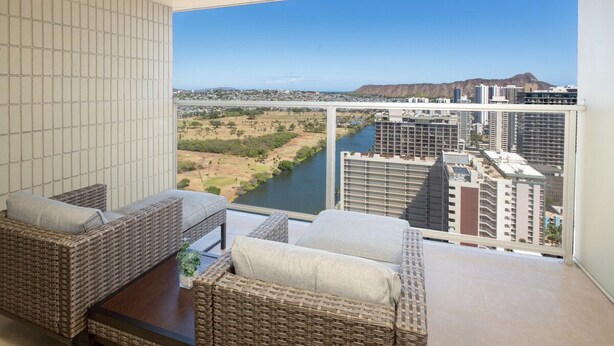Een balkon met rieten meubilair en uitzicht op een rivier en stadsbeeld.