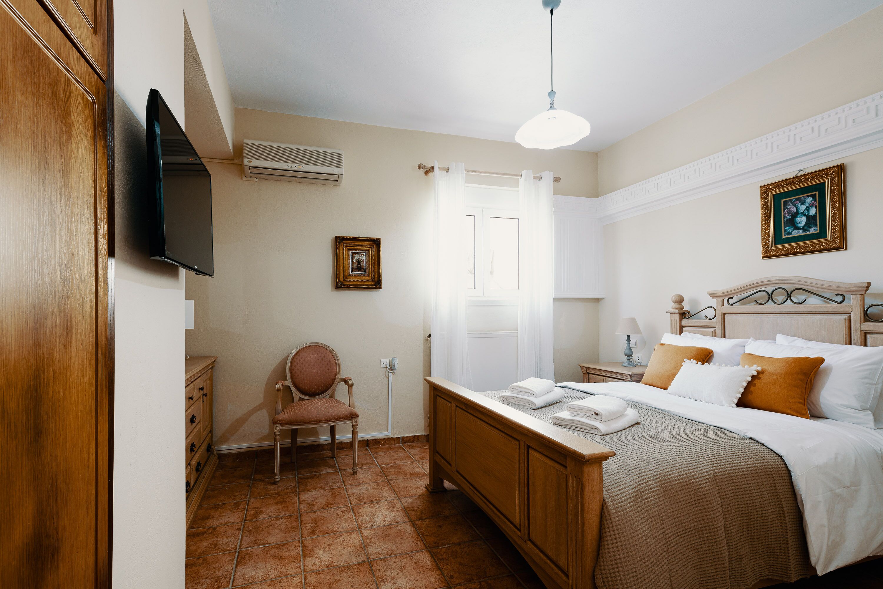 A bedroom with a bed, a chair, a bedside table, a TV, and a picture on the wall.