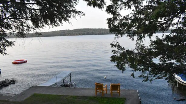 Une vue sur le lac, avec un quai, deux chaises en bois et un bateau gonflable rouge.