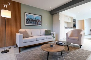 Una sala de estar moderna con un sofá, una mesa de centro redonda y una silla. Hay un cuadro en la pared y una lámpara en el suelo.