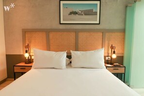 Habitación de hotel con una cama grande, dos mesitas de noche con lámparas, un cuadro enmarcado en la pared y un cabecero texturizado.