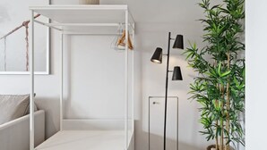 Habitación minimalista con una cama litera blanca, una lámpara de pie, una planta de bambú en maceta y un cuadro en la pared.
