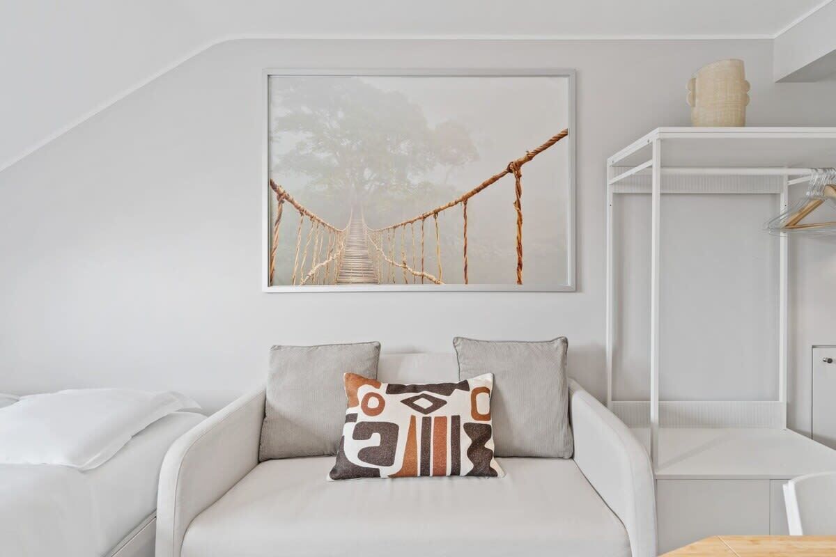 A modern room with a white sofa, a hanging artwork of a bridge, and a white cabinet with a hanging item.