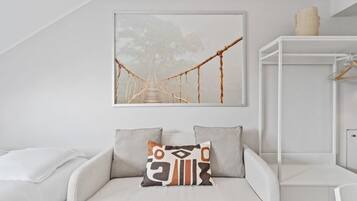 A modern room with a white sofa, a hanging artwork of a bridge, and a white cabinet with a hanging item.