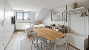 Habitación moderna y luminosa con una mesa de comedor de madera, sillas blancas, un sofá y un amplio ventanal que proporciona luz natural.