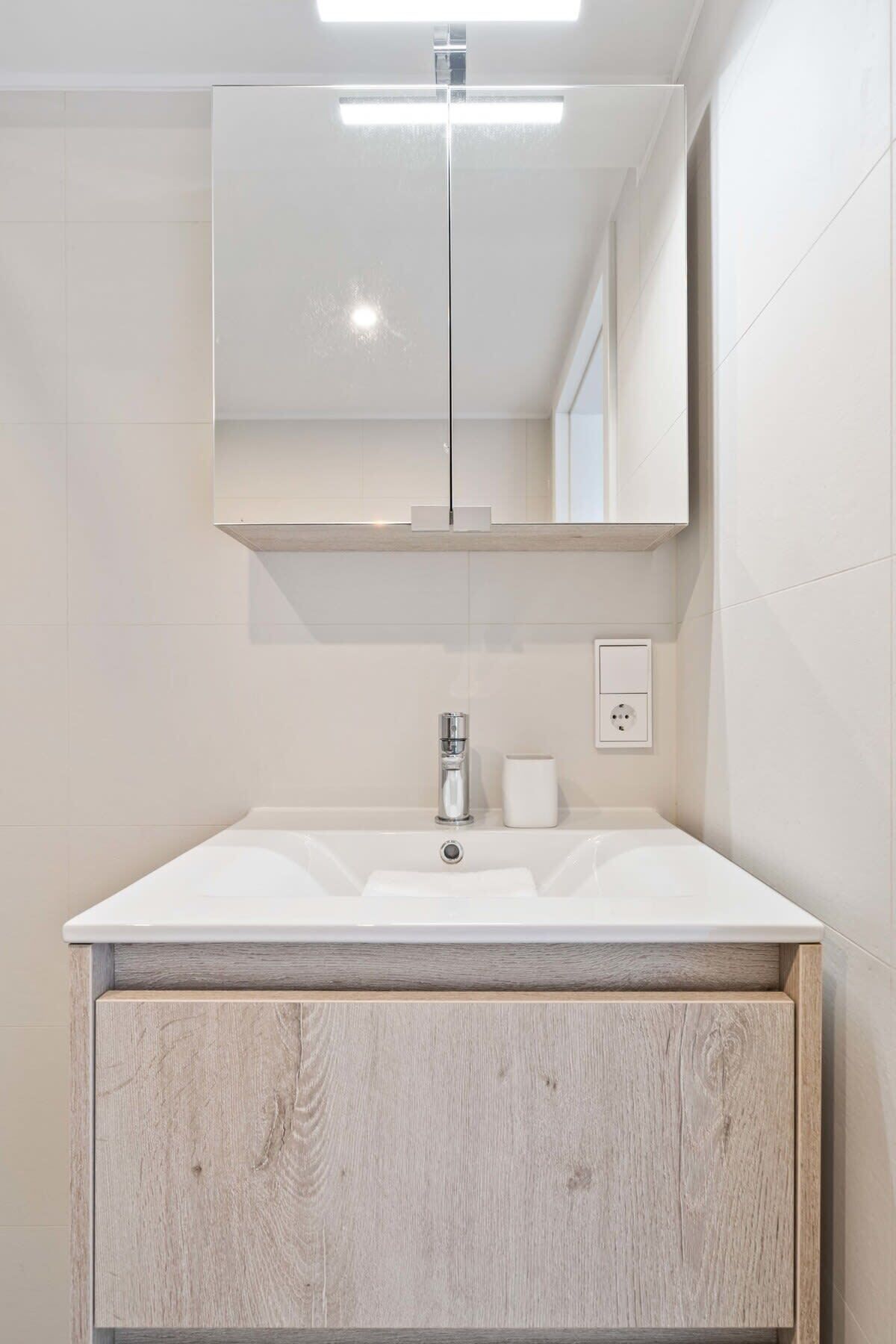 Un baño moderno con un lavabo blanco, un espejo encima y un mueble de madera debajo.