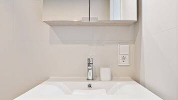 Un baño moderno con un lavabo blanco, un espejo encima y un mueble de madera debajo.